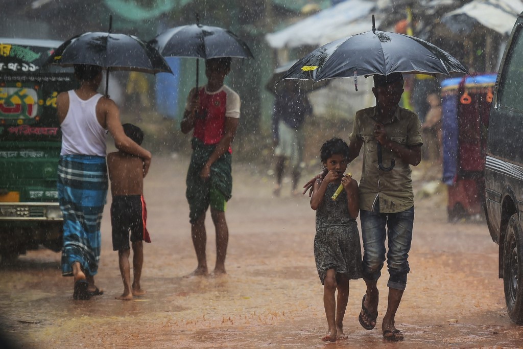 Rohingya refugees shelter under umbrellas as they walk along a path during a monsoon rainfall at Kutupalong refugee camp in Ukhia on July 23, 2019. (Munir Uz Zaman / AFP)