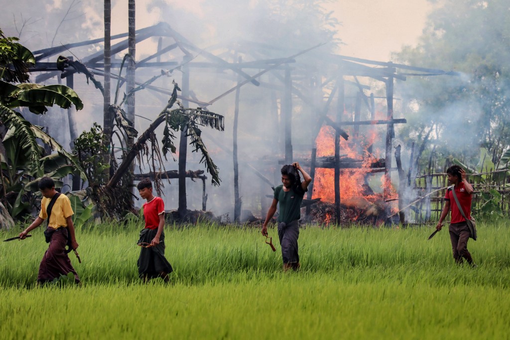 In this file photo taken on September 7, 2017 unidentified men carry knives and slingshots as they walk past a burning house in Gawdu Tharya village near Maungdaw in Rakhine state in northern Myanmar. (STR / AFP)
