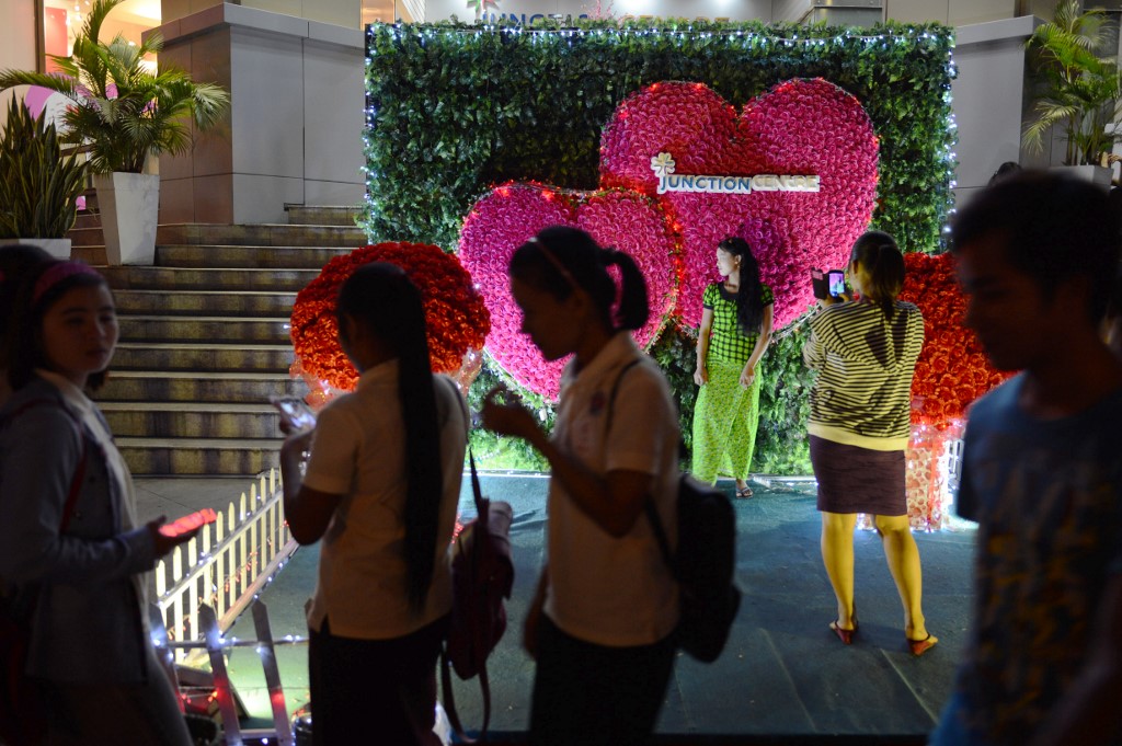 People pose for photograph in front of a valentine display of plastic flowers outside shopping mall Junction Centre in Yangon. (Romeo Gacad / AFP)