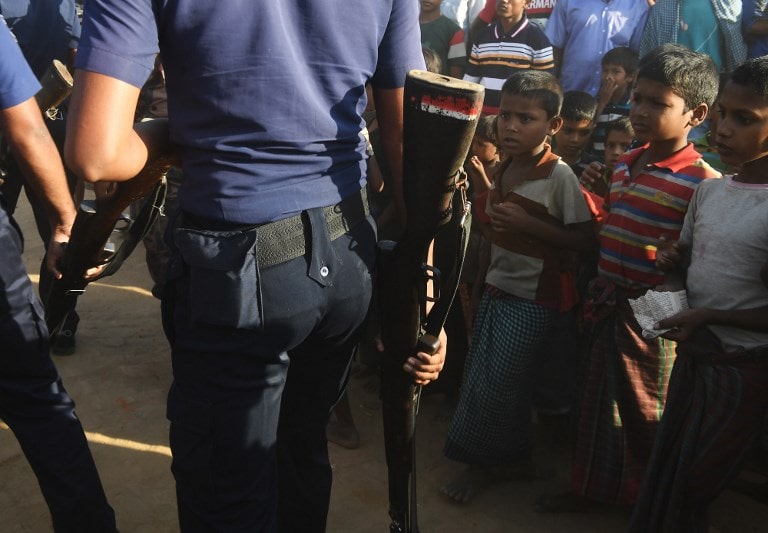 Rohingya refugees look on as Bangladeshi police officers walk past at the Unchiprang refugee camp near Teknaf. (Dibyangshu Sarkar / AFP)