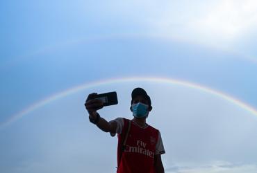 A man takes a selfie with the background of a rainbow on the sky following a rainfall in Yangon on May 1, 2020. (Ye Aung Thu / AFP)